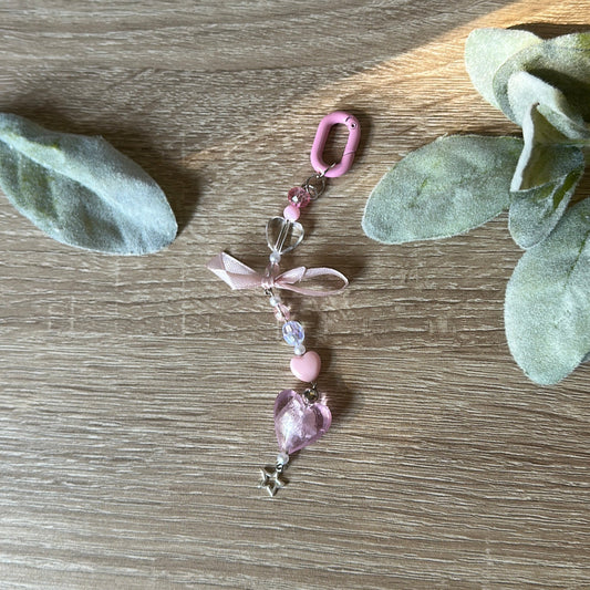 Decorative keychain with beads and ribbons on a wooden surface with green leaves.